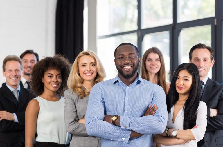 Diverse group of confident professionals posing together with a smiling man in the forefront in an office.