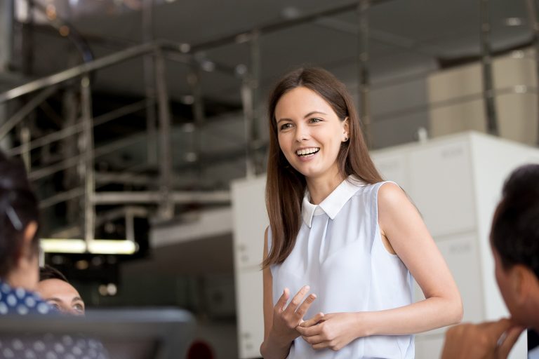 Confident young female leader speaking to colleagues in a bright, industrial office environment.