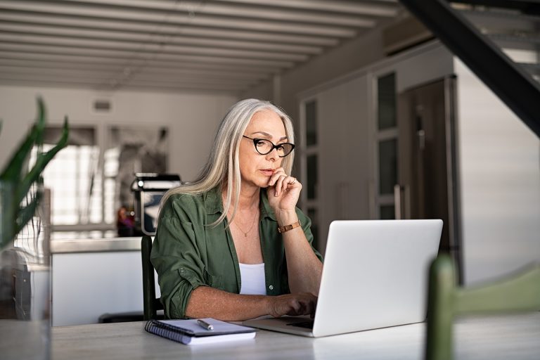 Mature professional woman working intently on her laptop at a stylish modern kitchen counter.