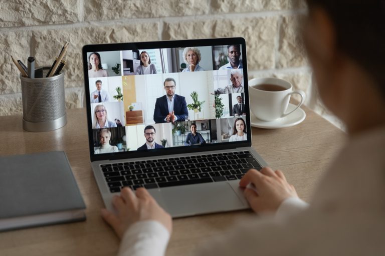 Woman participating in an online business meeting with multiple colleagues displayed on her laptop screen.