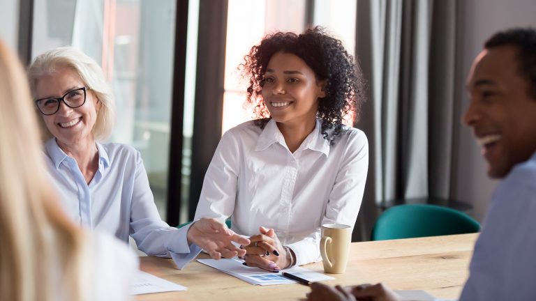 Diverse group of smiling professionals engaging in a lively discussion around a conference table.