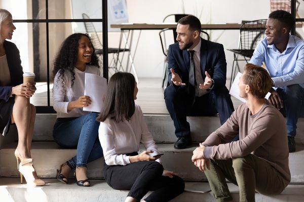 Casual business meeting with diverse employees laughing and discussing ideas on office steps.