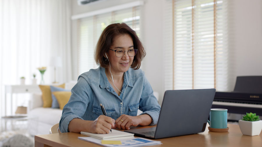 Focused woman taking notes while working on laptop in a home setting.