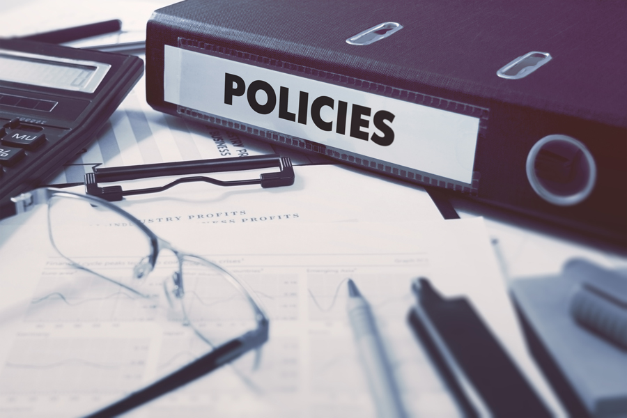 Business policies binder on a desk with financial reports and glasses.