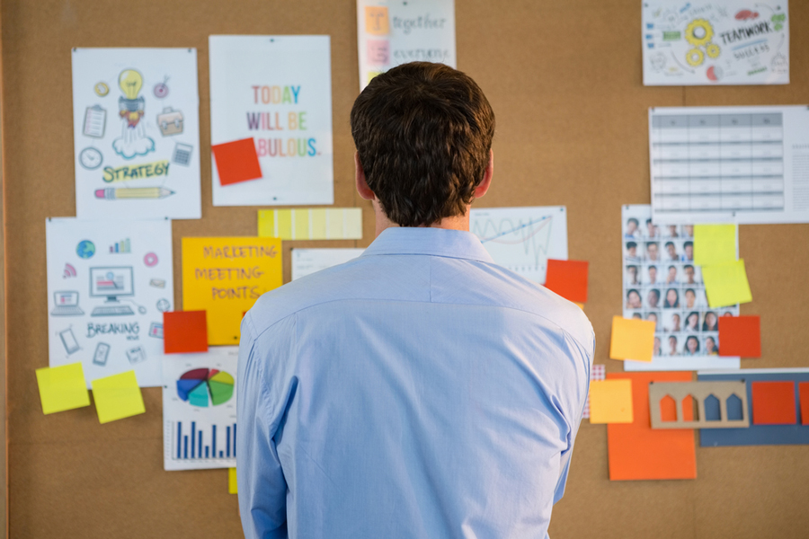 Man contemplating a bulletin board with strategy and teamwork posters in an office.