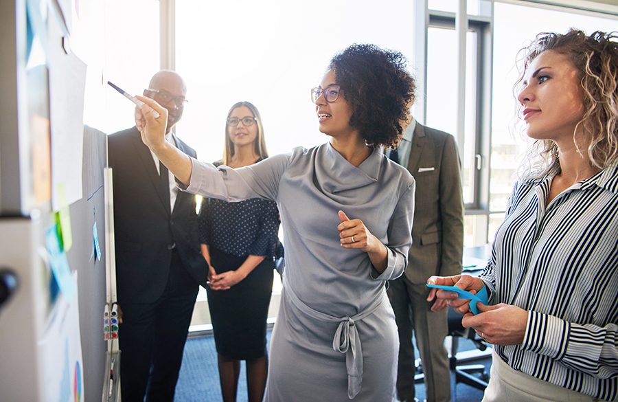 Diverse team engaging in a collaborative task with post-it notes on a glass wall.