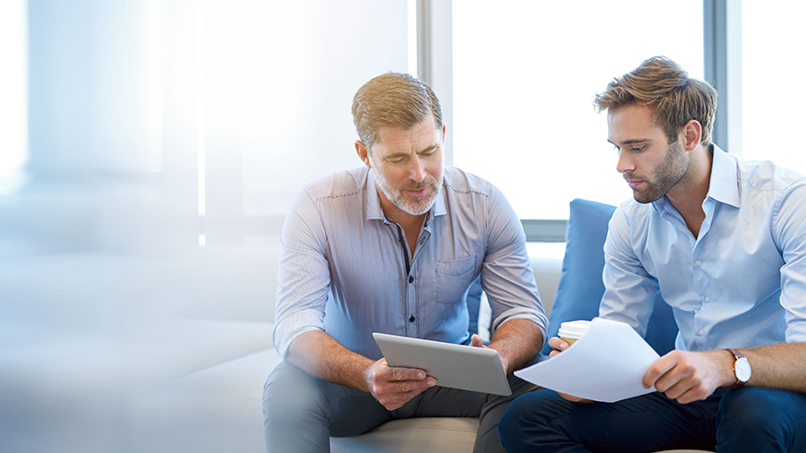 Two professionals reviewing digital content on a tablet in a bright office setting.