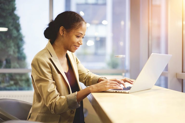 Professional woman happily working on laptop in a bright office setting.