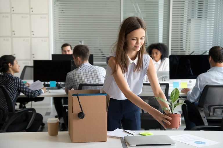 New employee settling into a busy office workspace with a plant and box of belongings.