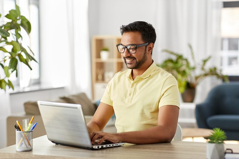 Smiling professional using laptop for online learning in a bright office setting.