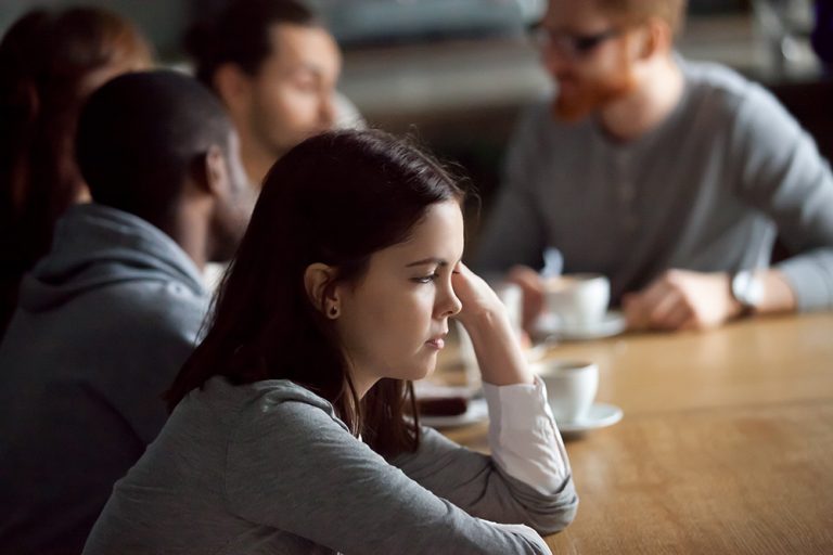 Thoughtful woman at a meeting with colleagues in the background.