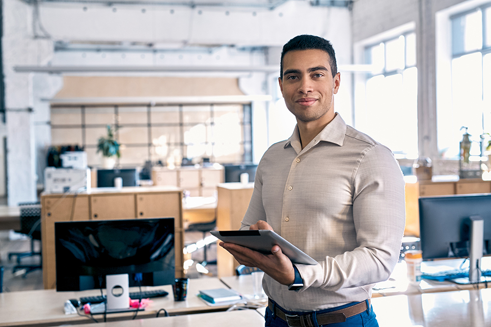 Confident professional holding a tablet in a modern office space.