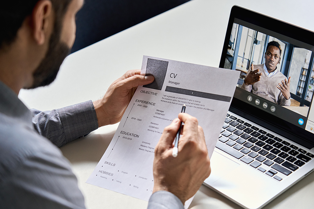 Professional reviewing a resume with a video interview candidate on laptop screen.