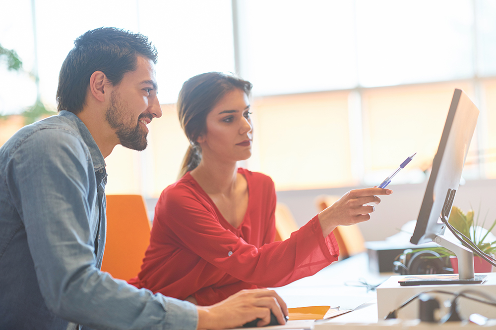 Two professionals discussing over computer screen in bright office.