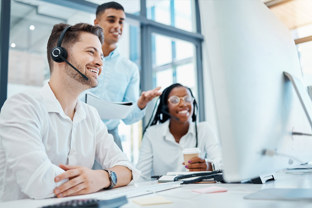 Smiling customer service team with headsets working at computers in modern office.