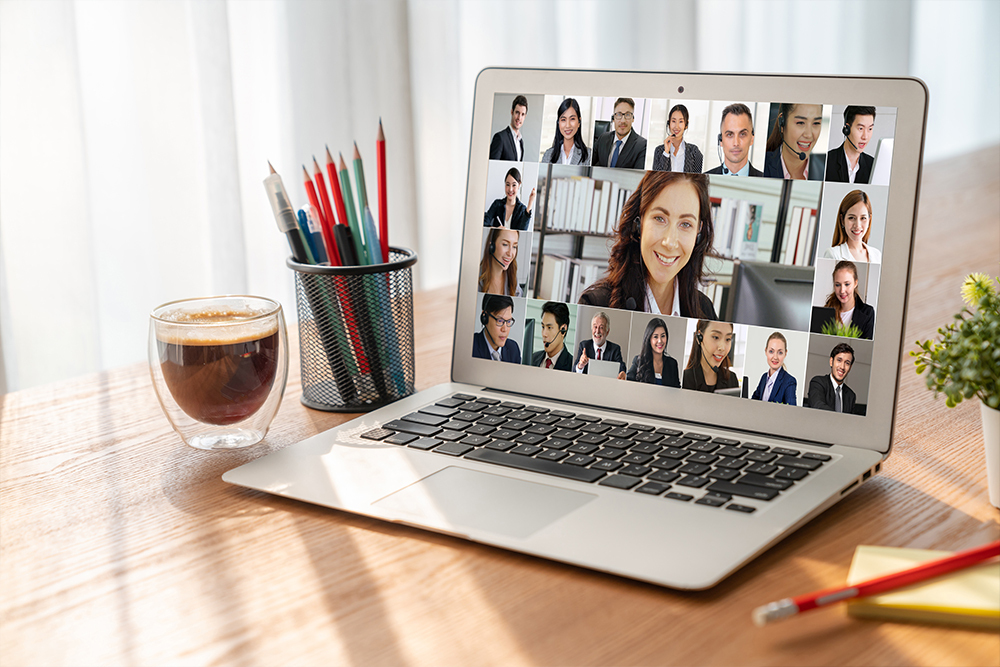 Laptop showing a virtual meeting with happy colleagues, coffee and stationery on desk.