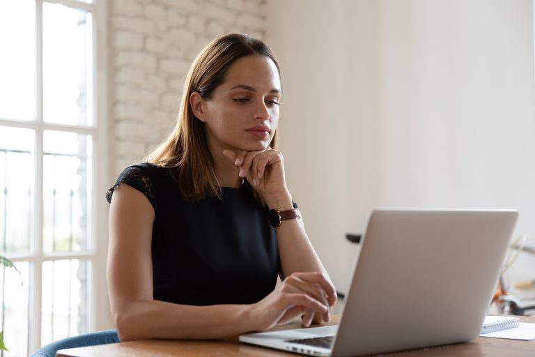 Focused woman working intently on a laptop in a bright, modern home office setting.