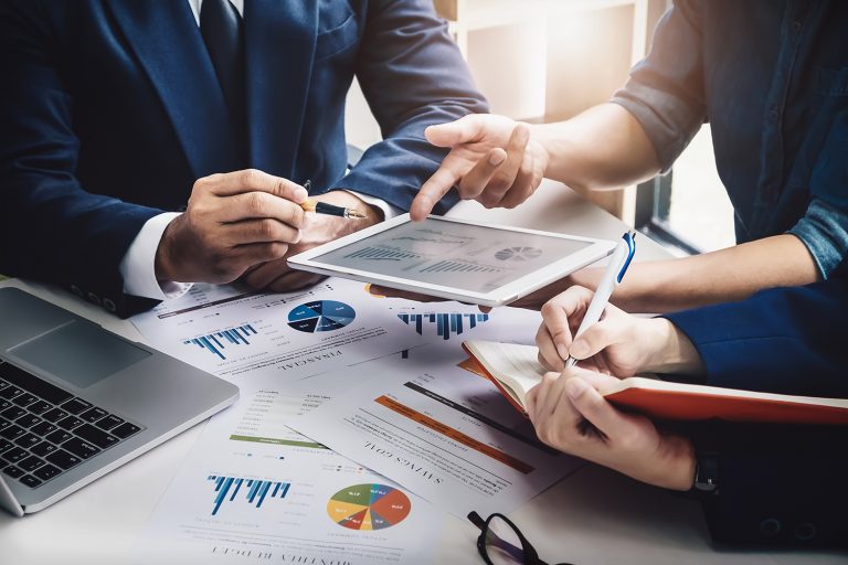 Close-up of business professionals analyzing financial data on a tablet over charts and graphs.