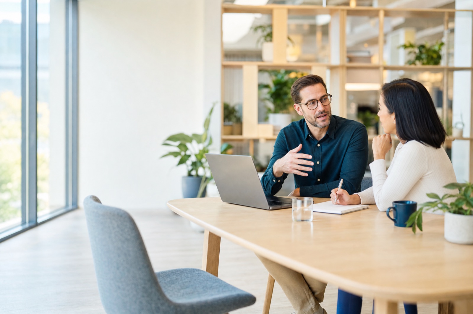 Eine Führungskraft und ein Recruiter besprechen an einem Tisch im hellen Büro eine offene Stelle, ihnen gegenüber ein leerer Stuhl