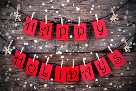 Red cards spelling 'HAPPY HOLIDAYS' hanging on a string with clothespins, against a wooden background with snowflakes.