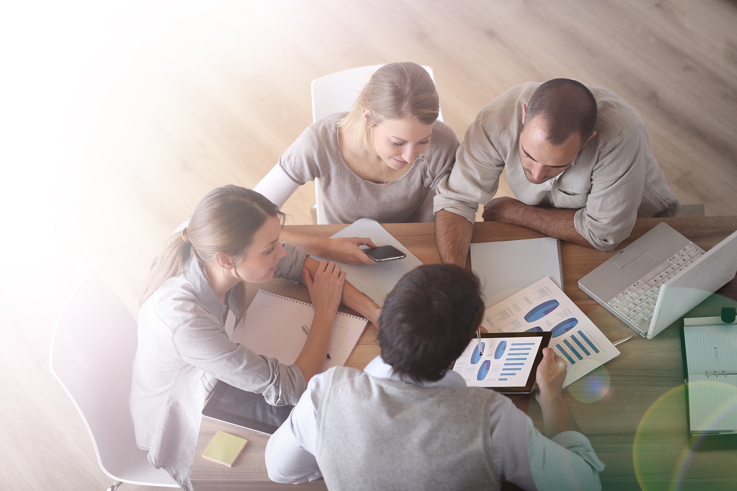 Overhead view of a team working together at a table, reviewing charts and data on a tablet and paper, symbolizing collaboration and teamwork.