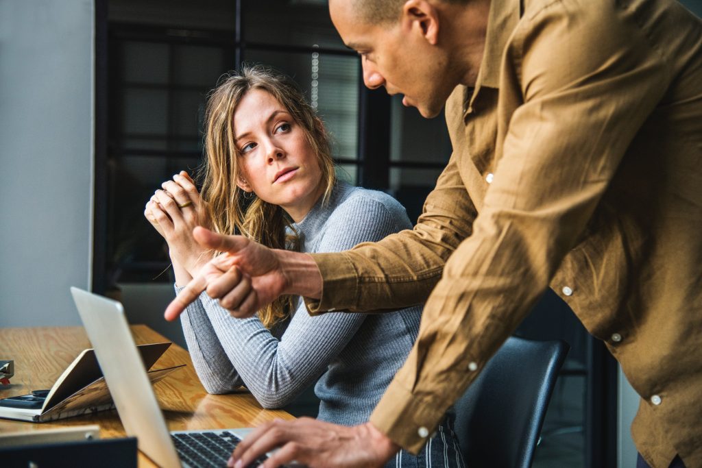 Woman listening to a male colleague explaining something on a laptop in the office.