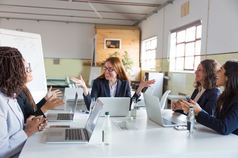 Happy team of diverse women in a lively discussion during a meeting in a modern office.