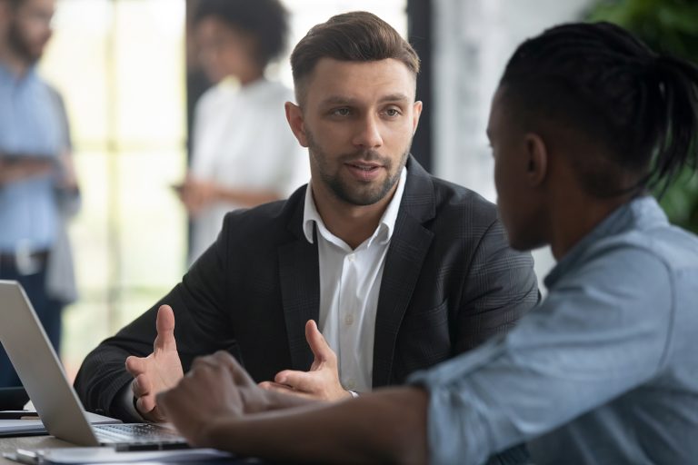 Two male colleagues having a serious discussion while working on a laptop in the office.