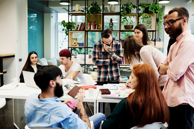 Dynamic group of young professionals collaborating around a cluttered table in a modern office space.