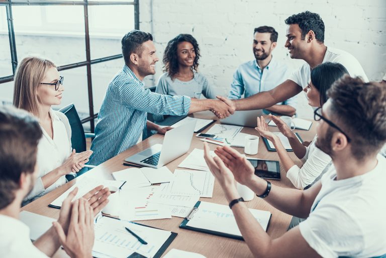 Enthusiastic business team celebrating a successful agreement with a handshake in a modern office.