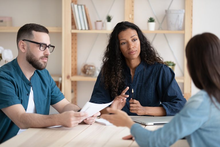 Three professionals discussing documents at a table in a bright, modern office setting.