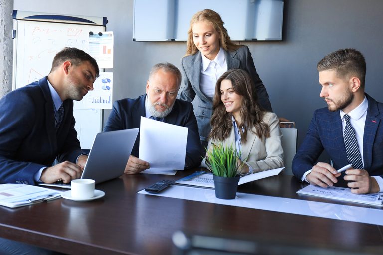 Business professionals engaged in a strategic discussion with documents and laptops at a boardroom table.