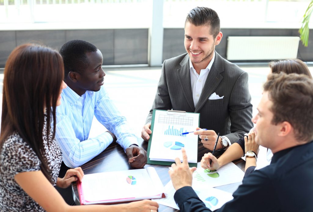 Diverse group of professionals engaging in a discussion with charts and graphs at a meeting.
