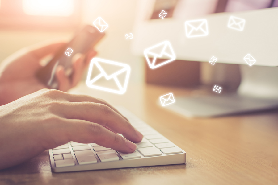 Person typing on a keyboard with digital email icons floating above.
