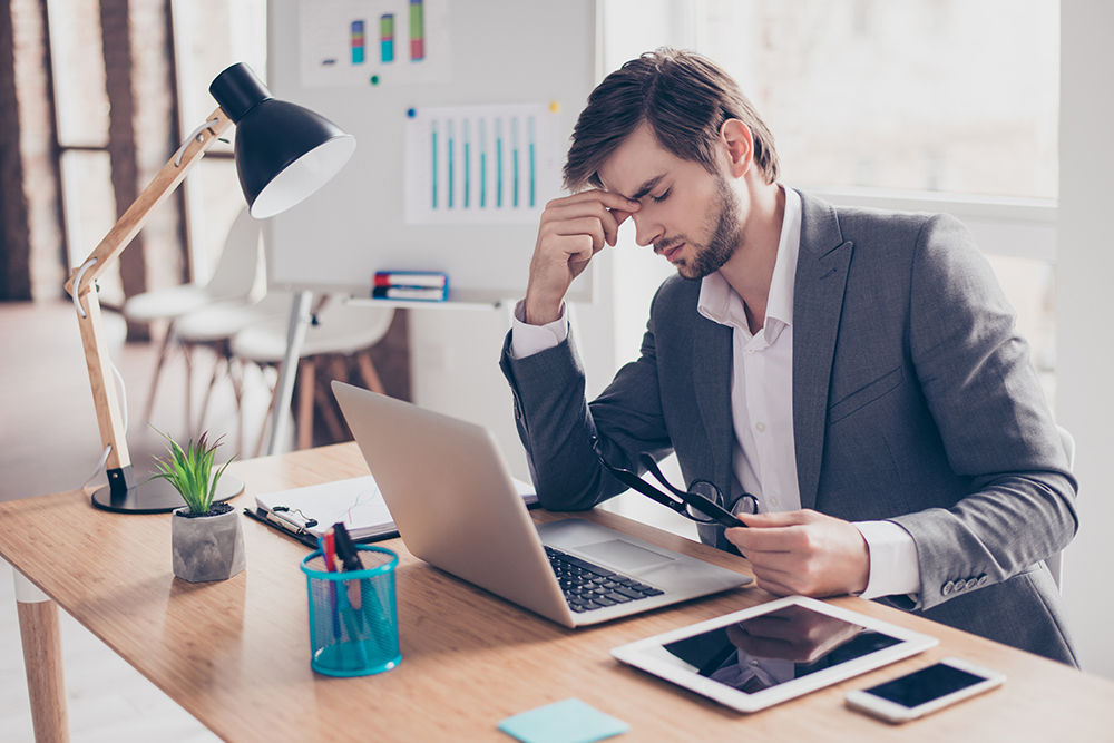 Stressed businessman with glasses at a cluttered desk.