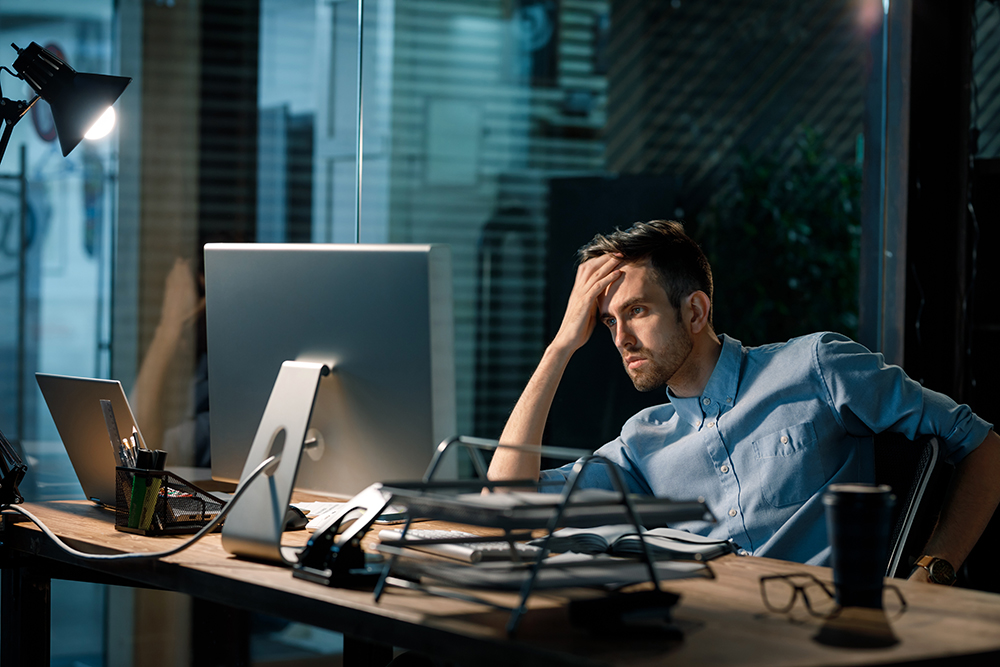 Overwhelmed man at desk with multiple screens during nighttime.