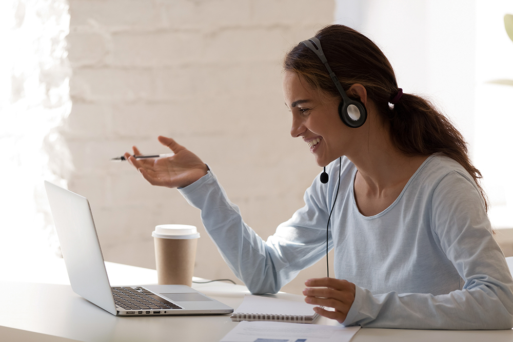 Cheerful woman with headset gesturing during a video call on laptop.