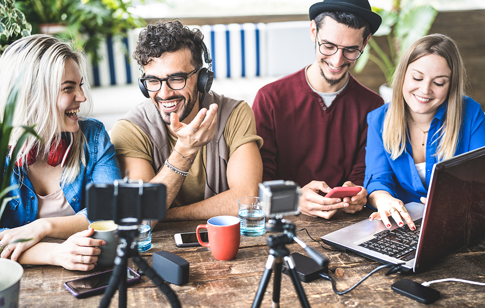 Joyful young team conducting a video call with a smartphone and laptop at a casual office meeting.