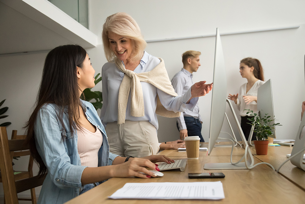Senior manager conversing with a young employee in a bright office environment.