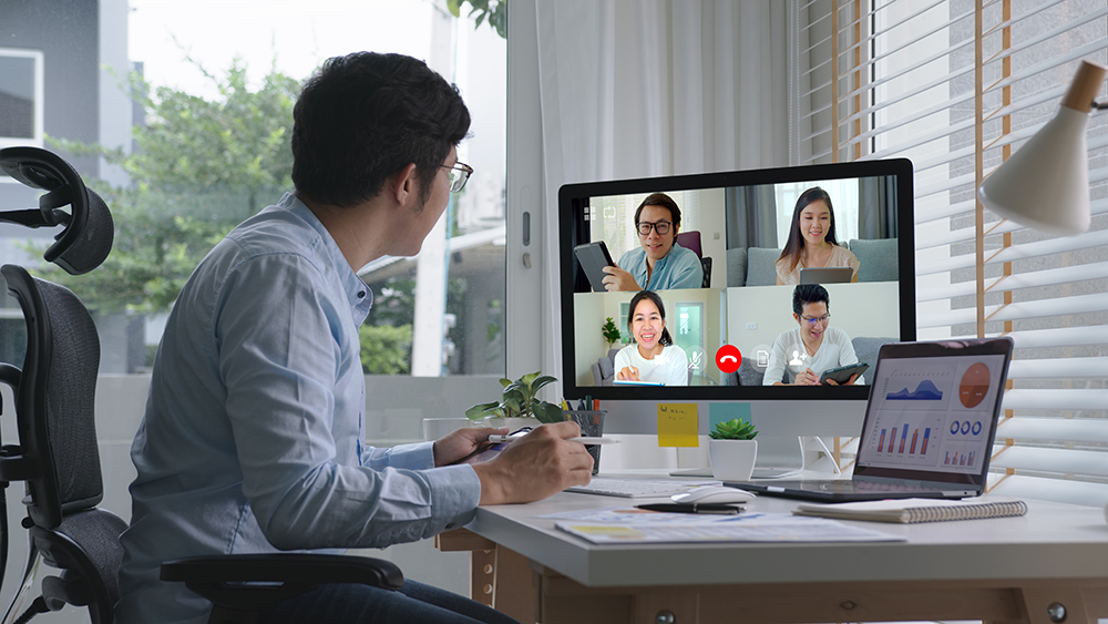 Man in a video call with five colleagues on a desktop screen in a modern office.