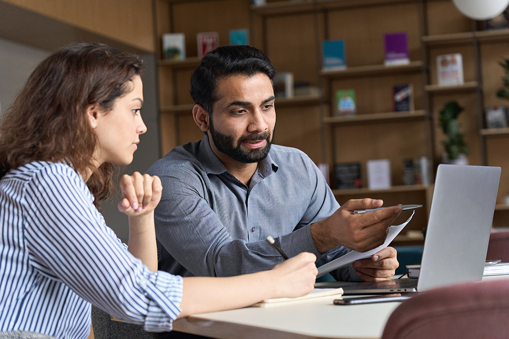 Focused coworkers discussing over laptop in a well-organized office space.
