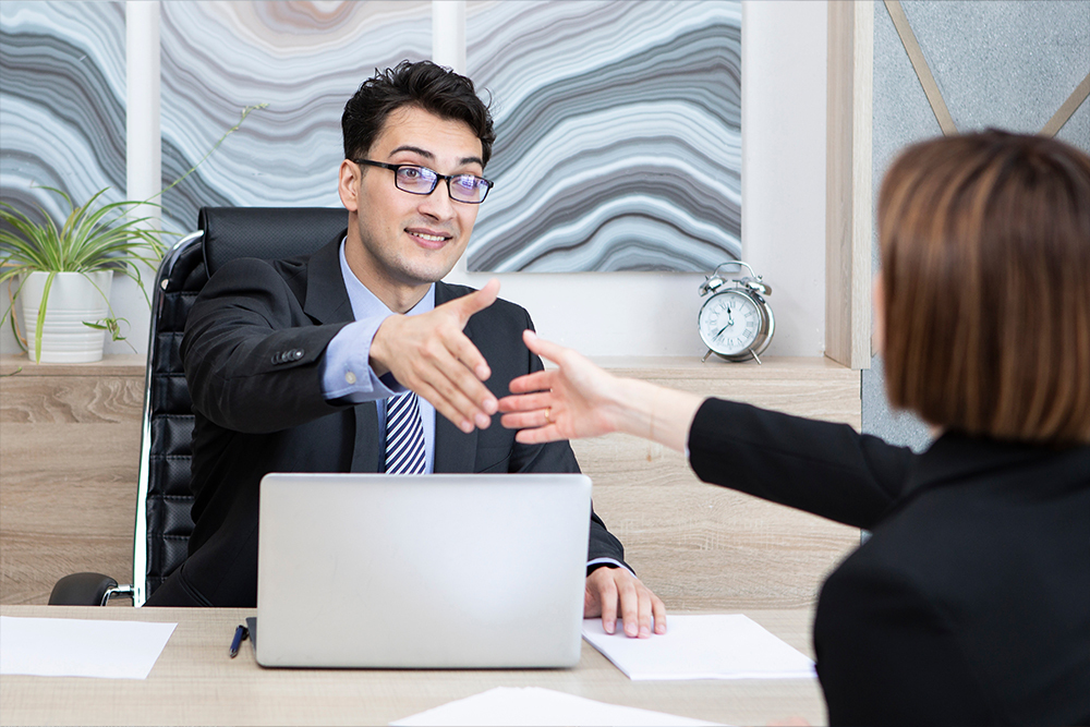 Confident businessman offering a handshake across the desk during an interview.